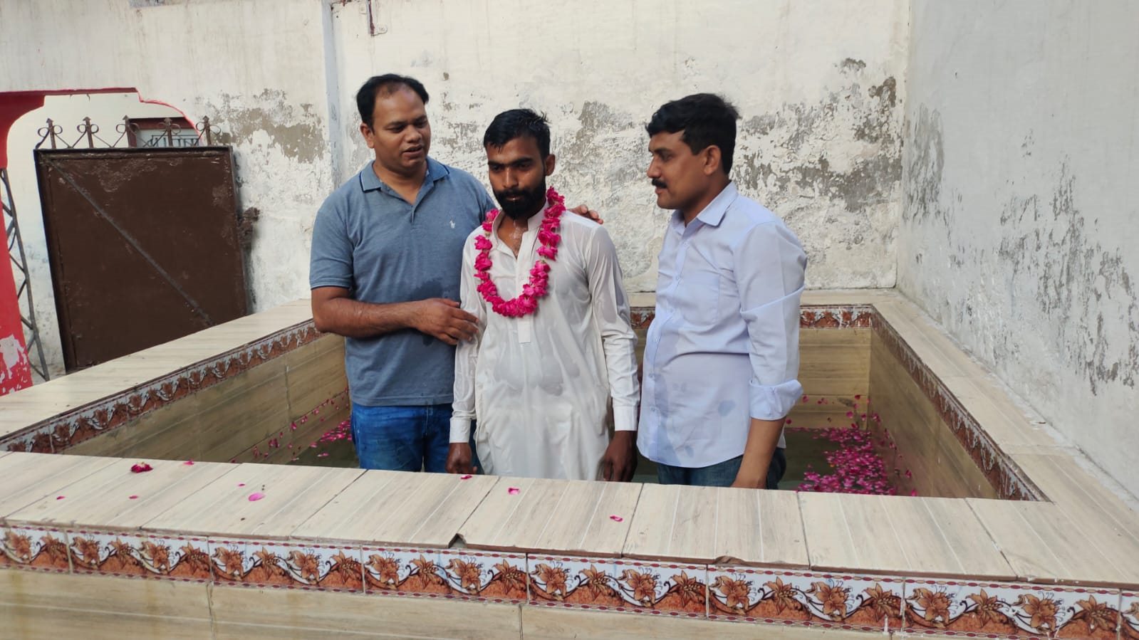 A baptism candidate with ministry leaders at a tiled baptism pool