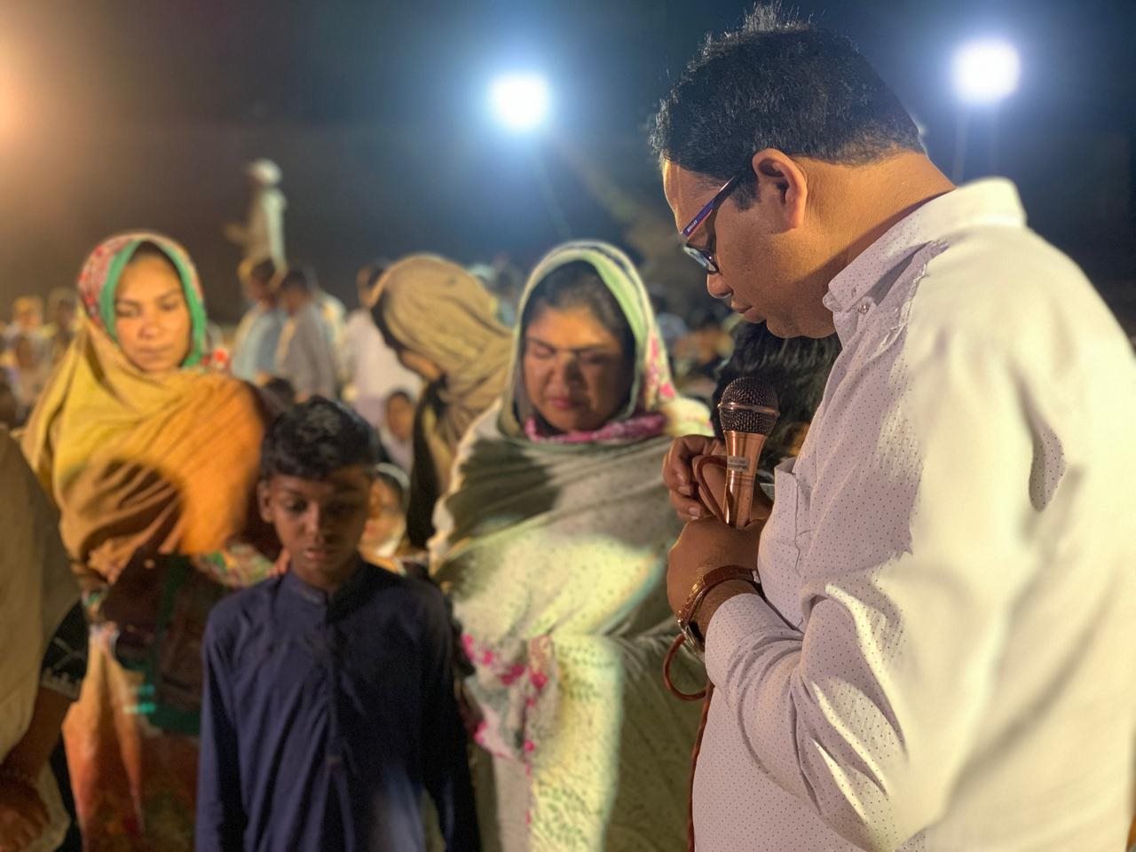A speaker praying with people at an evening gathering